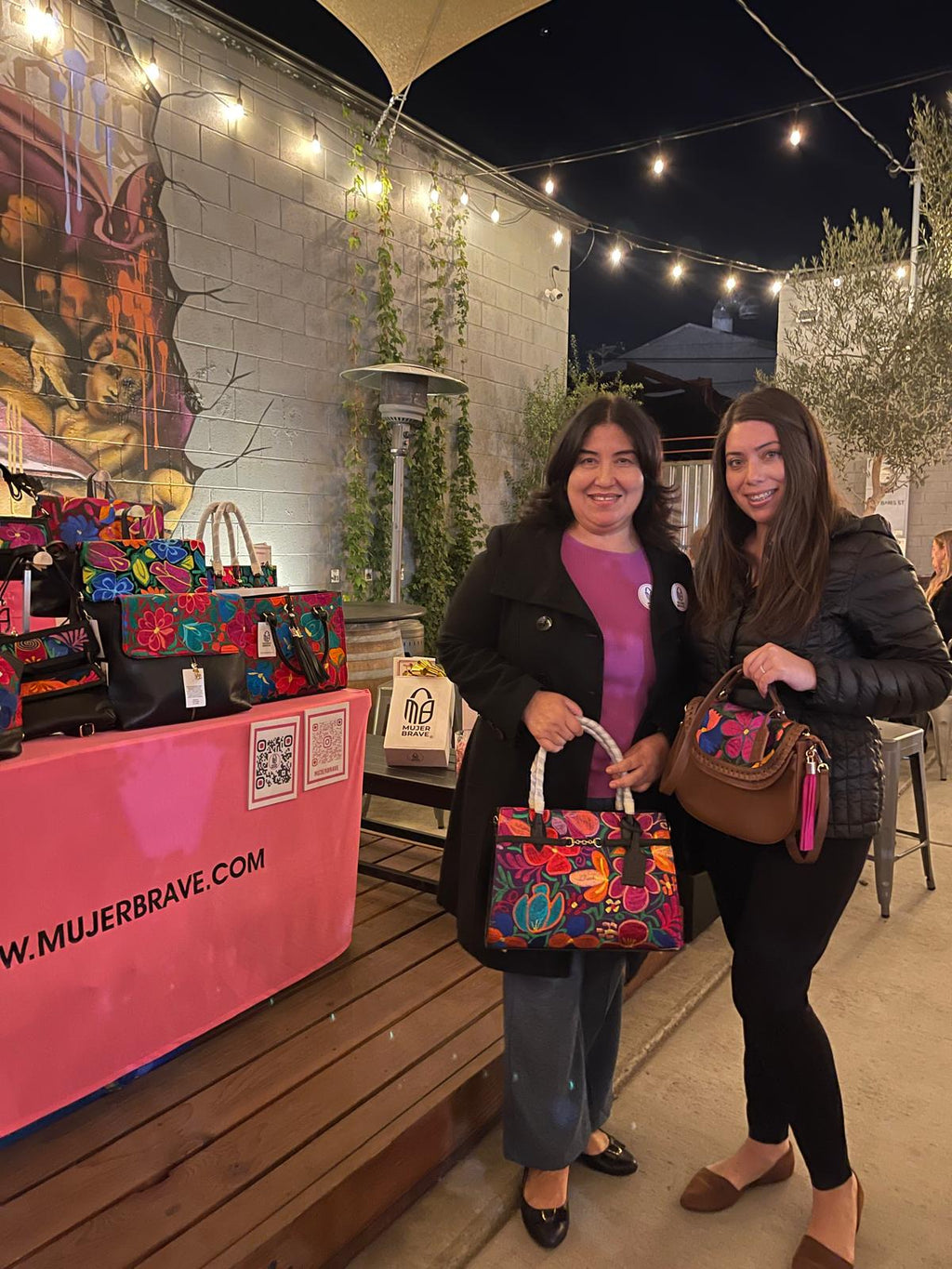 women posing for pic and showcasing embroidered leather handbags